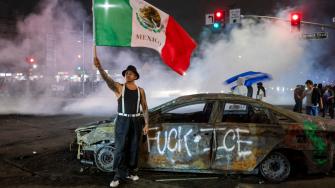 Un manifestante ondea la bandera mexicana junto a los restos de un auto quemado, pintado con grafitis contra el Servicio de Inmigración y Control de Aduanas de Estados Unidos (ICE).