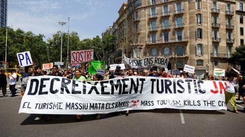 Personas sostienen una pancarta que dice "Disminuir el turismo ya" durante una protesta contra el turismo masivo, en Barcelona, ​​España.